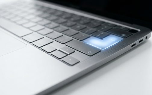 Ezüst laptop billentyűzete kék világító gombbal a fehér asztalon.