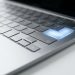 Ezüst laptop billentyűzete kék világító gombbal a fehér asztalon.